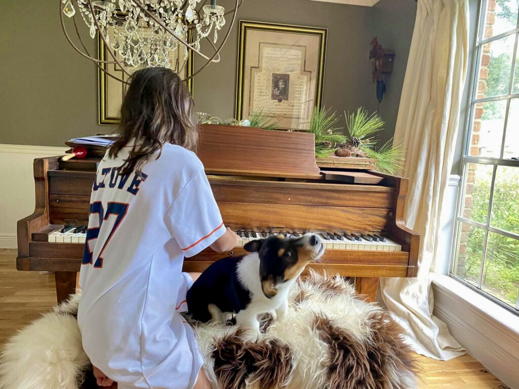 A dog named Gatsby singing along while a girl plays the piano.